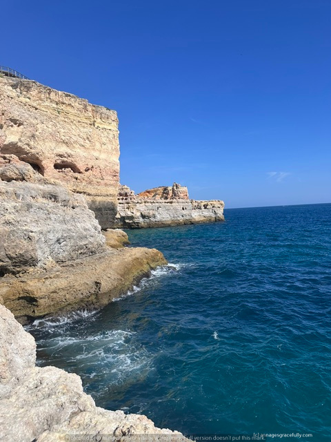 Uitzicht op rotsachtige kust met helderblauw water onder een heldere lucht.