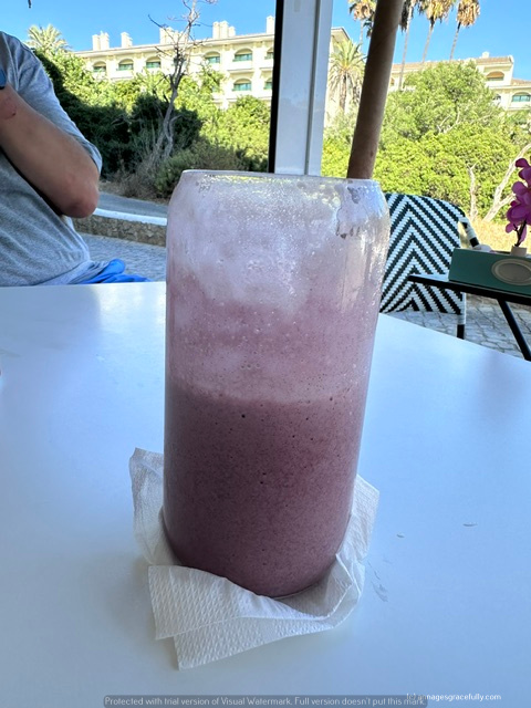 Een glas met een paarse smoothie op een tafeltje, omringd door een groene omgeving.