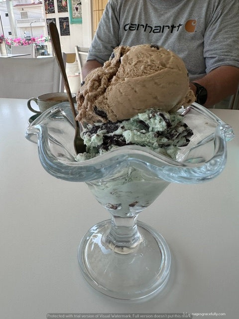 Een grote ijscoupe met scheppen van chocolade- en muntsmaakijs, geserveerd in een glazen schaaltje met een lepel.