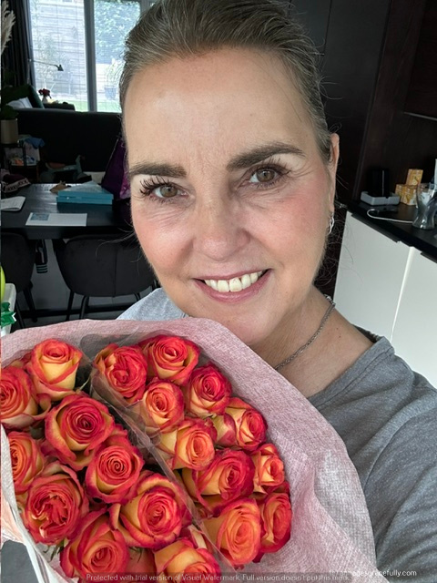 Vrouw die glimlachend een boeket met oranje en roze rozen vasthoudt.