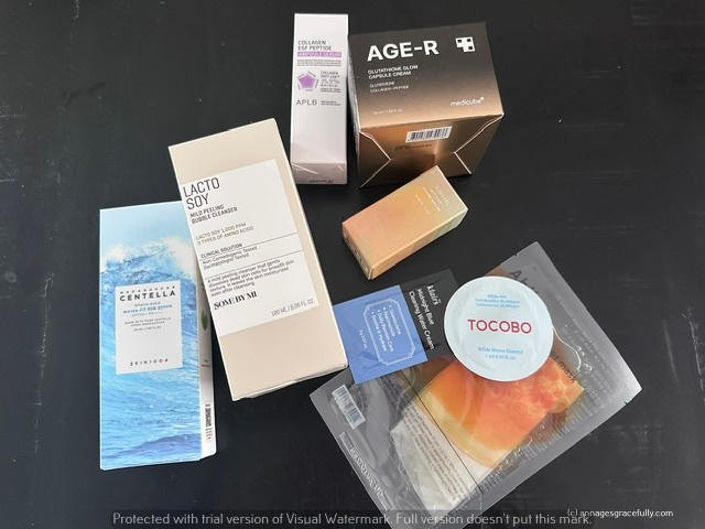 Een verzameling huidverzorgingsproducten en cosmetica verpakkingen op een zwarte ondergrond. Producten omvatten Lacto Soy, Centella, AGE-R, Aple, en Tocobo.