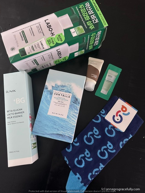 Een samenstelling van verschillende huidverzorgingsproducten, waaronder een fles iUNIK Beta-Glucan Lacto Barrier Milk Essence, een SkinDog Centella huidverzorgingsproduct, een kleine tube crème en een paar sokken met een logo en patroon.