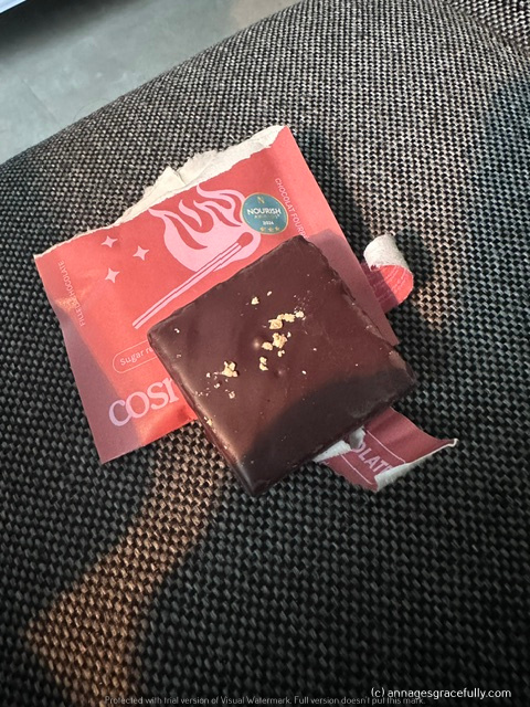 Een stuk chocolade op een rood verpakkingspapier, liggend op een gestreepte ondergrond.