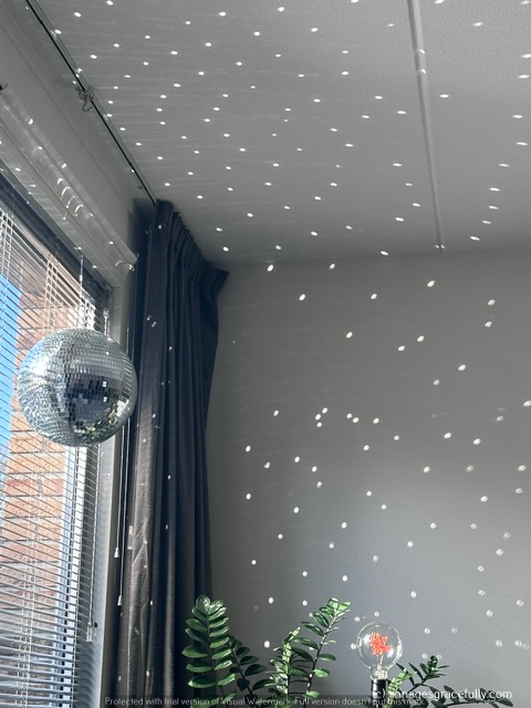 Een spiegelbal hangt aan het plafond, met lichtreflecties die een sprankelend effect creëren op de muur en het plafond van een kamer.