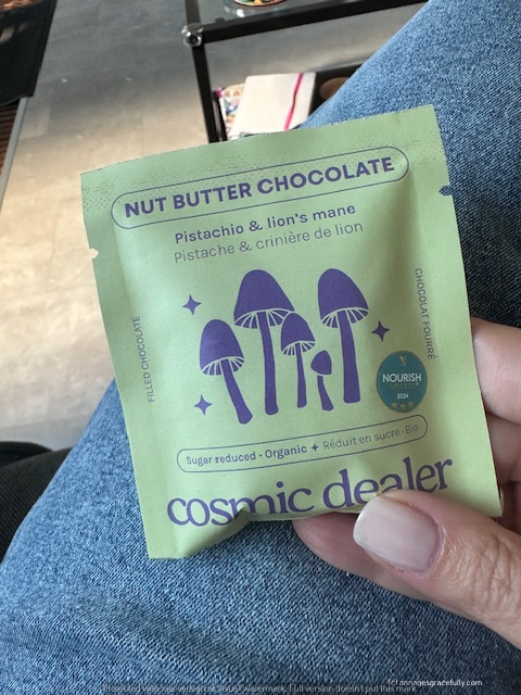 Verpakking van 'Nut Butter Chocolate' met smaken pistache en lion's mane, gepresenteerd door Cosmic Dealer. Groene verpakking met illustraties van paddestoelen.