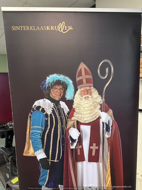 Een promotiereclame met Sinterklaas en Zwarte Piet, beide gekleed in traditionele kostuums met een feestelijke achtergrond.
