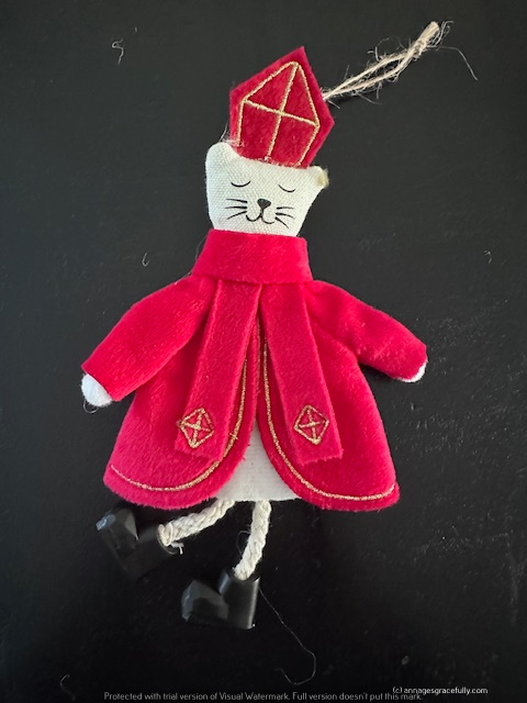 Een schattige handgemaakte kat in een rode mantel en mijter, hangend aan een touw.