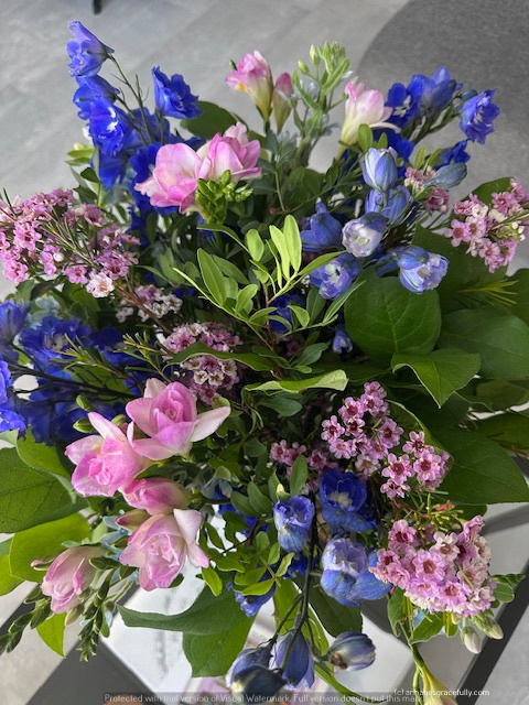 Een kleurrijk boeket met roze, paarse en blauwe bloemen, omringd door groen bladeren.